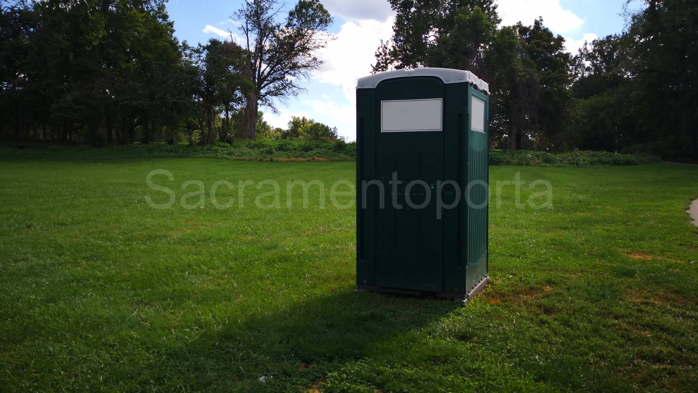 A portable toilet in a park surrounded by trees. Renting Versus Buying A Portable Potty